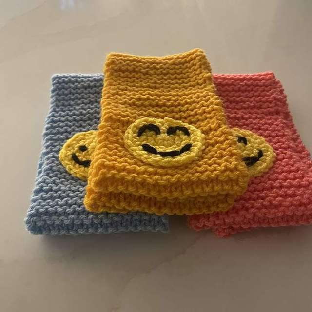 Three handmade kids crochet scarves in blue, yellow, and coral with smiley face patches